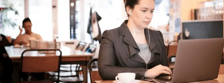Woman in professional attire sitting on laptop working in a busy public space