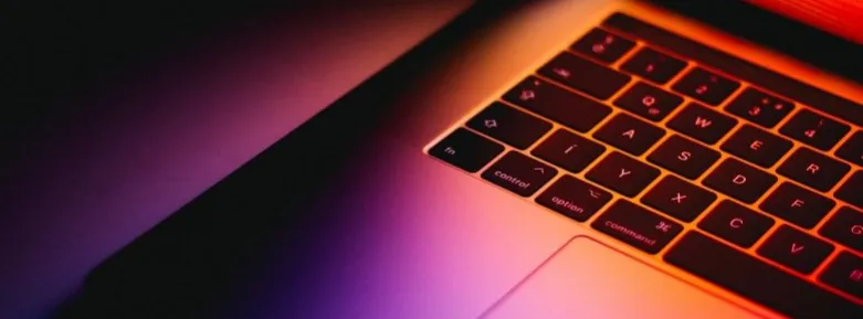 A half-open laptop lit from behind in purple and red