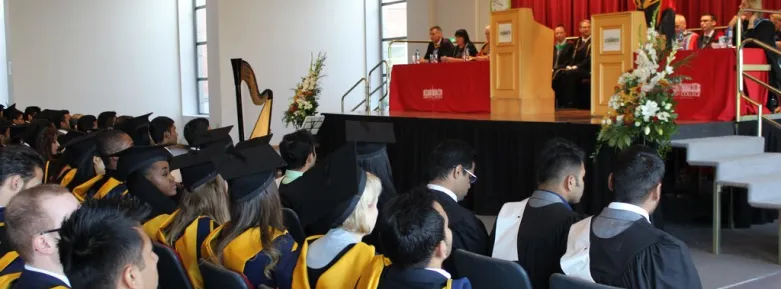 Several rows of graduates in cap & gowns look up at a raised dais with a speaker at a Griffith College graduation ceremony