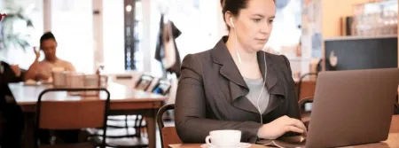 Woman in professional attire sitting on laptop working in a busy public space