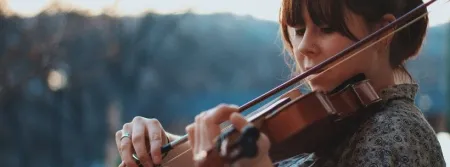 A young woman playing violin on a balcony with trees in the background
