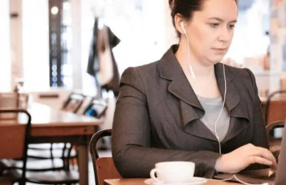 Woman in professional attire sitting on laptop working in a busy public space