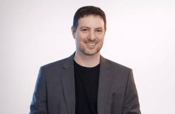 a man wearing a suit and tie smiling at the camera
