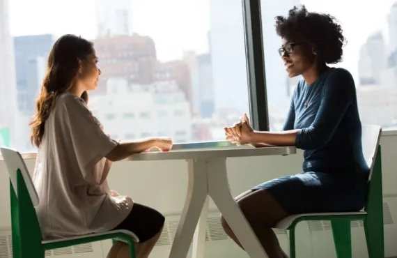 Two women sitting at a table in front of a window, conducting an interview
