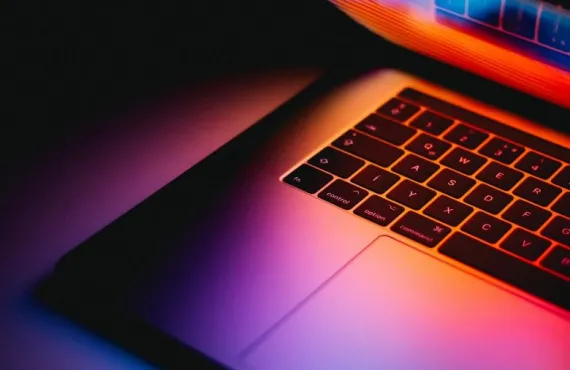 A half-open laptop lit from behind in purple and red