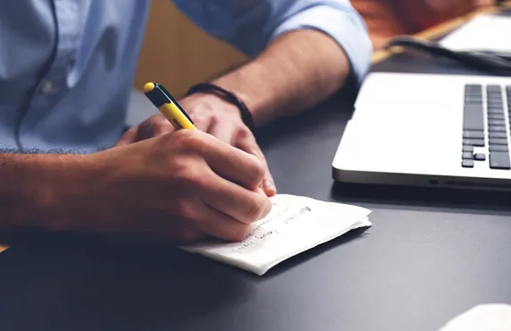 Man taking notes with laptop open