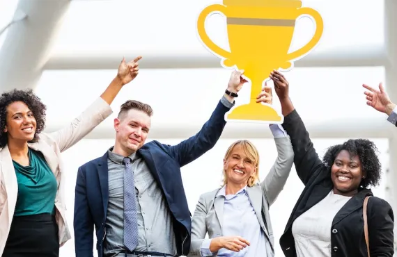 A thrilled team points to an oversize cut-out of a trophy