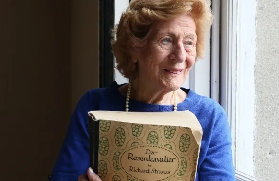 Irish opera singer Veronica Dunne stands at a window, holding a copy of the score of Richard Strauss's Der Rosenkavalier