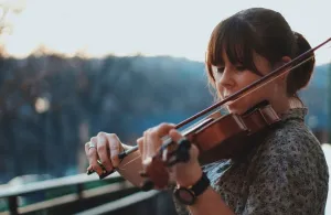 A young woman playing violin on a balcony with trees in the background