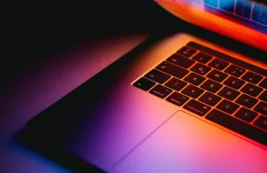 A half-open laptop lit from behind in purple and red