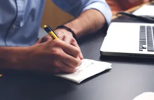 Man taking notes with laptop open