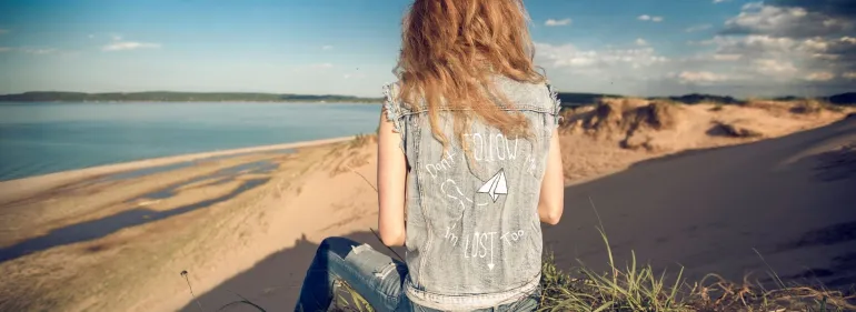 A young woman faces away from the camera looking at a beach and the horizon