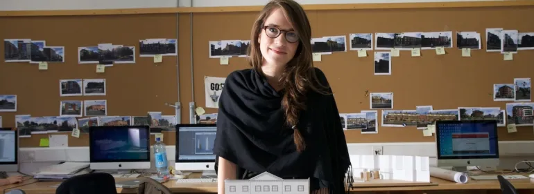 A female architecture student stands smiling behind a model of her work