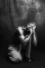 Black and white image of crouched performer on dark stage with head bowed and hands over face.