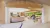    Pictured is a café with a counter and seating, filled with people. There are beams on the ceiling and a moss installation, as well as bespoke lighting. 