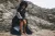 Model sitting on rough coastal rock, in long denim coat with stripe silk chiffon embellishment on báinín sleeves.