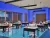 A 3D architectural render of a modern classroom with vibrant blue walls and a patterned blue floor. The room is furnished with navy student desks featuring white tops and bright red chairs on wheels. Long, black pendant lights hang from the ceiling.