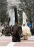 Tall, fur‑covered festival figures with vivid masks parade outdoors before a gathered crowd. 
