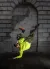 A person in a neon yellow hoodie performs a one-handed freeze, legs kicked up in the air, against a gray stone archway. 