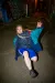 A person with long braids in a blue windbreaker and shorts holds a low floor pose in a graffiti-covered alley at night.