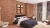 Boutique hotel bedroom with brick wallpaper, navy bedding, patterned curtains and lounge seating.