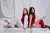 Two models sitting on a bed, back to back, wearing a red dress, and a red and white outfit