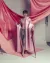  A shirtless figure draped in pink satin stands against flowing fabric, holding an ornate sword in a theatrical studio portrait.