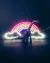 A toy dinosaur stands silhouetted in front of a glowing rainbow neon light in a darkened scene.