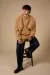 Model sits on stool wearing an oversized camel crewneck and a pair of jeans while holding a rose in front of a beige background