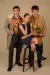 Three models pose in a studio against a beige background, on the left a male model wears a grey overcoat, a female model is seated on a stool in the middle and to her right stands a male model in an oversized camel crewneck