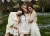 Three models standing together in a flower field dressed in wool and sheer silk outfits.