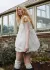 Model in bubble dress walking away and looking to the side with a small greenhouse in the background.