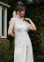 Model in a sheer top with raw seamlines and gathered trousers standing with her hand on her shoulder. 