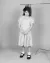 A young child stands in a dress beneath a clothing rail, with sections of hair tied upward to the bar in a surreal studio portrait.