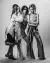 Three models wearing flowing satin and silk outfits with lace detailing, against a white backdrop