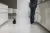 A small black rabbit sits on a kitchen floor beside a person standing at a counter in a bright modern home.