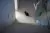  A small black rabbit sits alone on a tiled floor at the bottom of a staircase in soft natural light. 