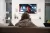 A person in a hoodie sits on a sofa smoking while watching television in a dimly lit living room.
