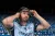 A hurler in a Dublin jersey adjusts a helmet while standing in a stadium with rows of blue seats in the background.