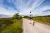 Photo from behind of a man running down a long dirt road
