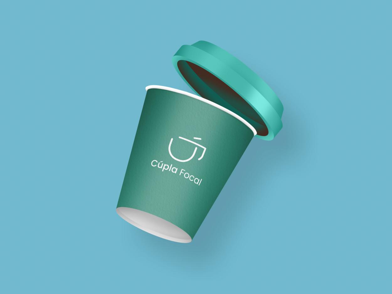 This coffee cup showcases the Cúpla Focal branding applied to takeaway packaging, displaying the recognisability of the logo across physical products. The muted green and blue palette represents the national colour of Ireland (blue) and the green earth of the country (green). The clean white logo maintains a modern and approachable aesthetic.