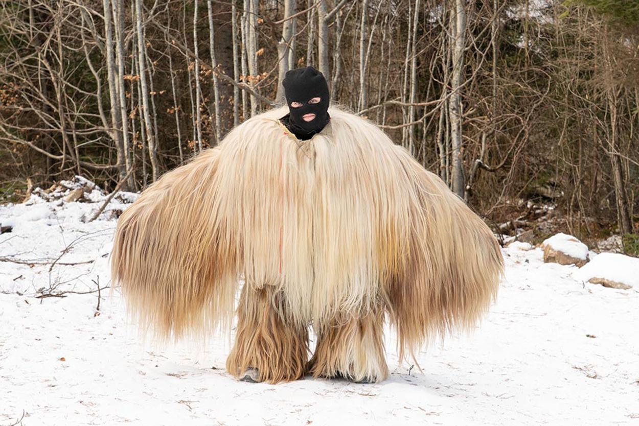 A person wearing an enormous shaggy fur-like costume stands in a snowy forest
