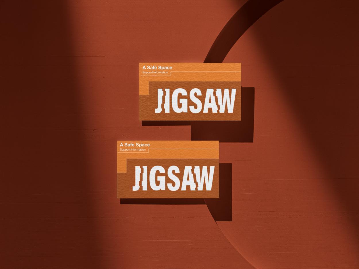 9-	2 Jigsaw support card fronts displayed on an orange wall,  the front contains a large Jigsaw logo and “A Safe Space – Support Information”