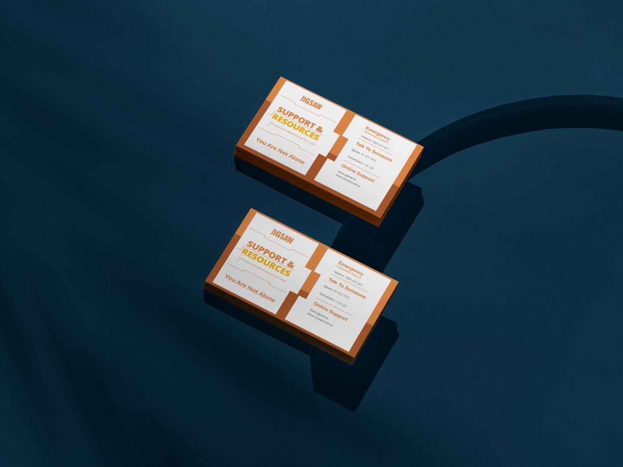 10-	2 orange Jigsaw support card backs are displayed on a blue table, the cards contain contact information including Jigsaw’s website, phone lines as well as the Samaritan’s Helpline