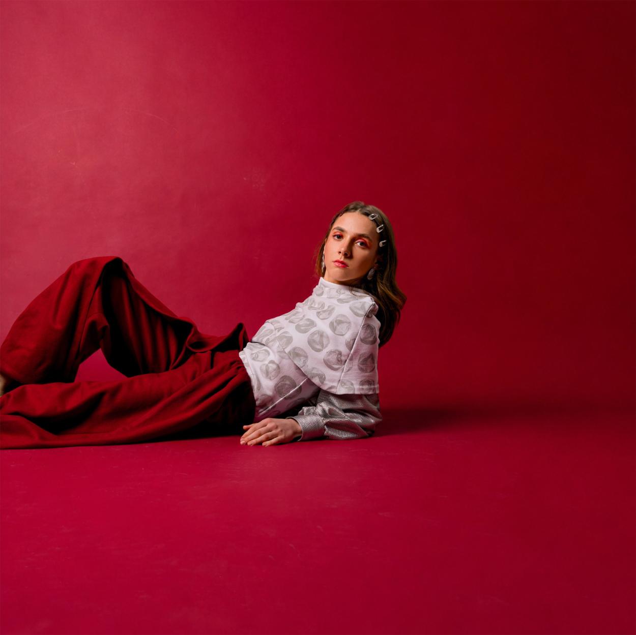Model in front of red backdrop wearing red wool pants and a white and silver shirt