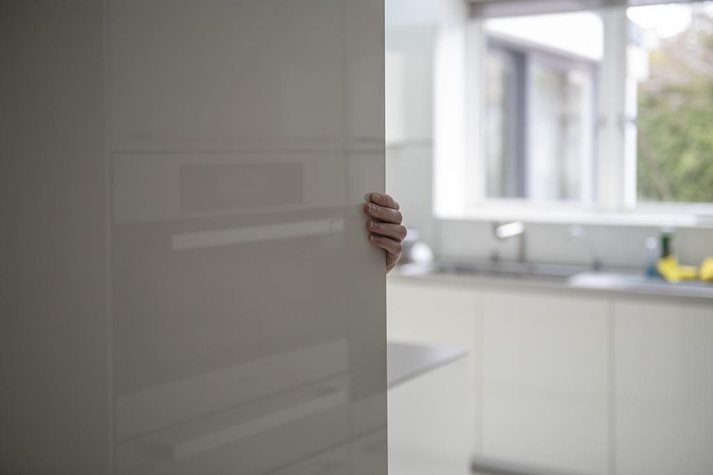 A hand grips the edge of a partially opened kitchen cabinet door in a softly lit interior.