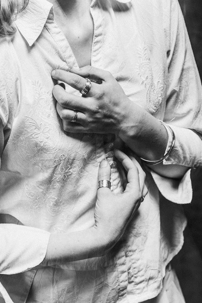 Black and white image of close-up of hands gripping the front of an embroidered shirt.