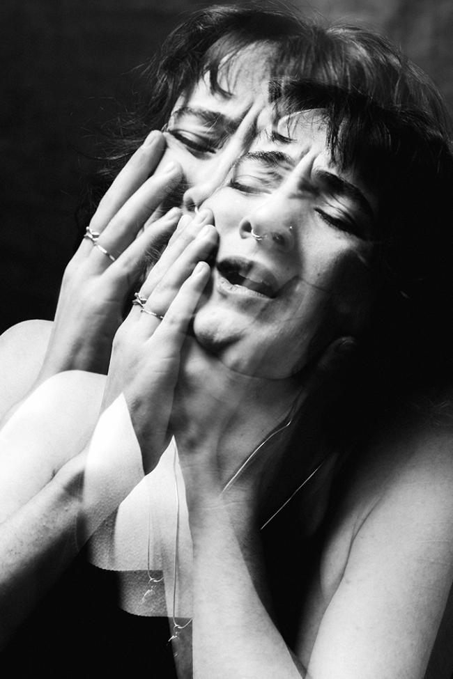 Black and white image of a performer’s face and hands shown in a blurred, overlapping motion effect.