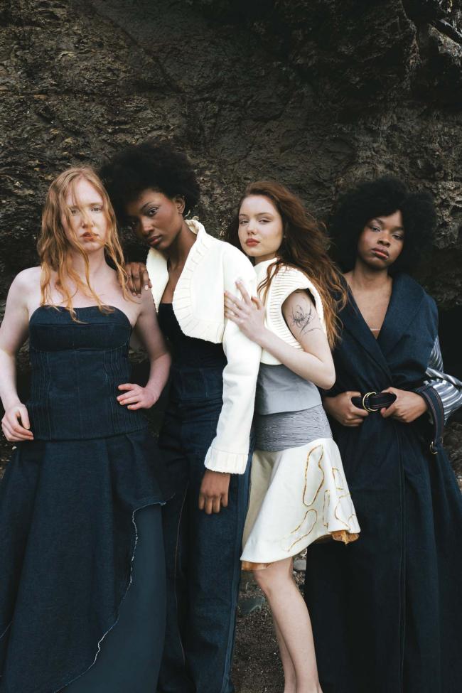 Four Models in wearing outfits of denim, cream wool báinín, and grey cotton, featuring fabric manipulation mimicking the background of the rough coastal rock in background.