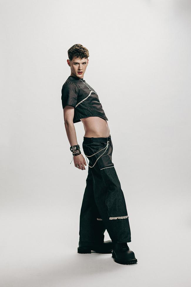 Male model wearing a black denim top and black denim jeans with a chain and black boots.